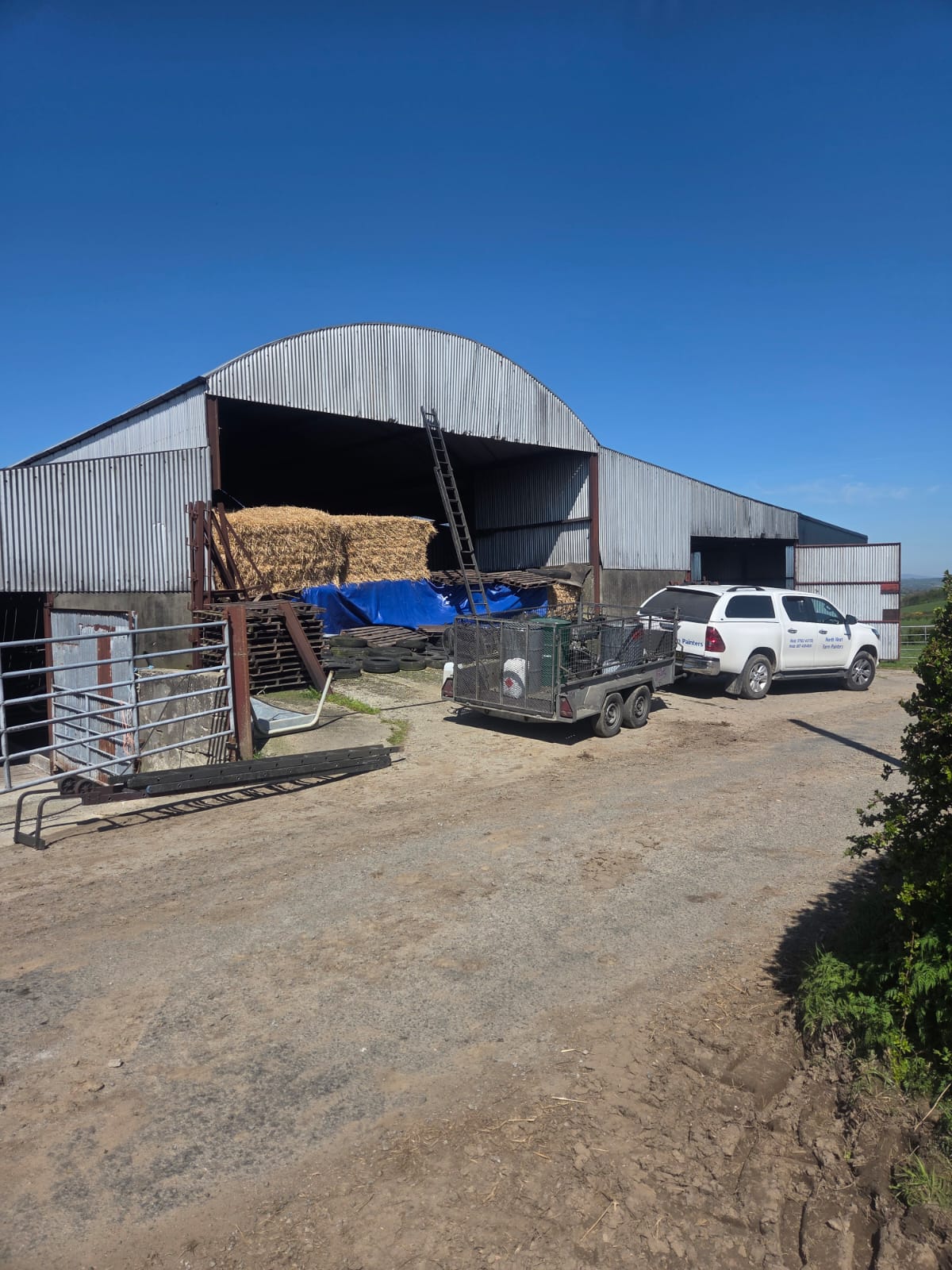 Corrugated barn with hay bales and Northwest Farm Sprayers van on a sunny day