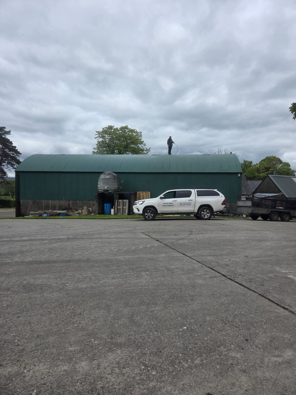 Green painted farm shed with Northwest Farm Sprayers van and worker on roof