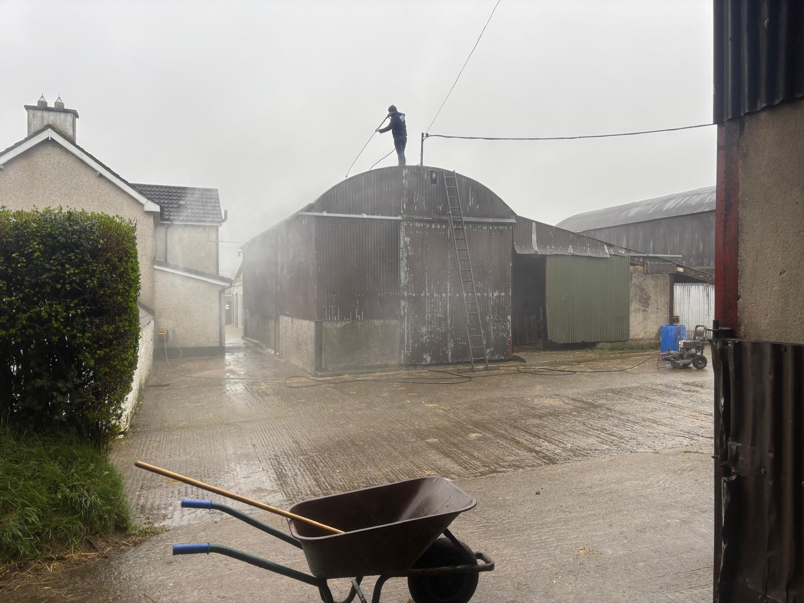 Worker power washing a barn roof before painting
