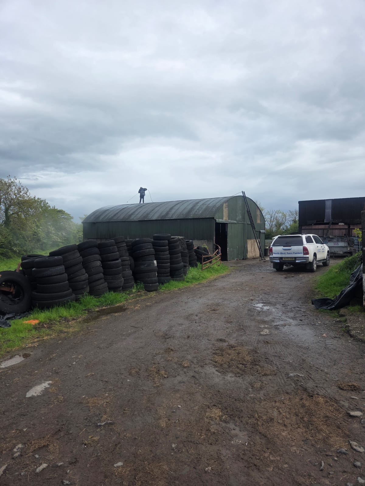 Worker spray painting a green farm shed roof with company van parked outside