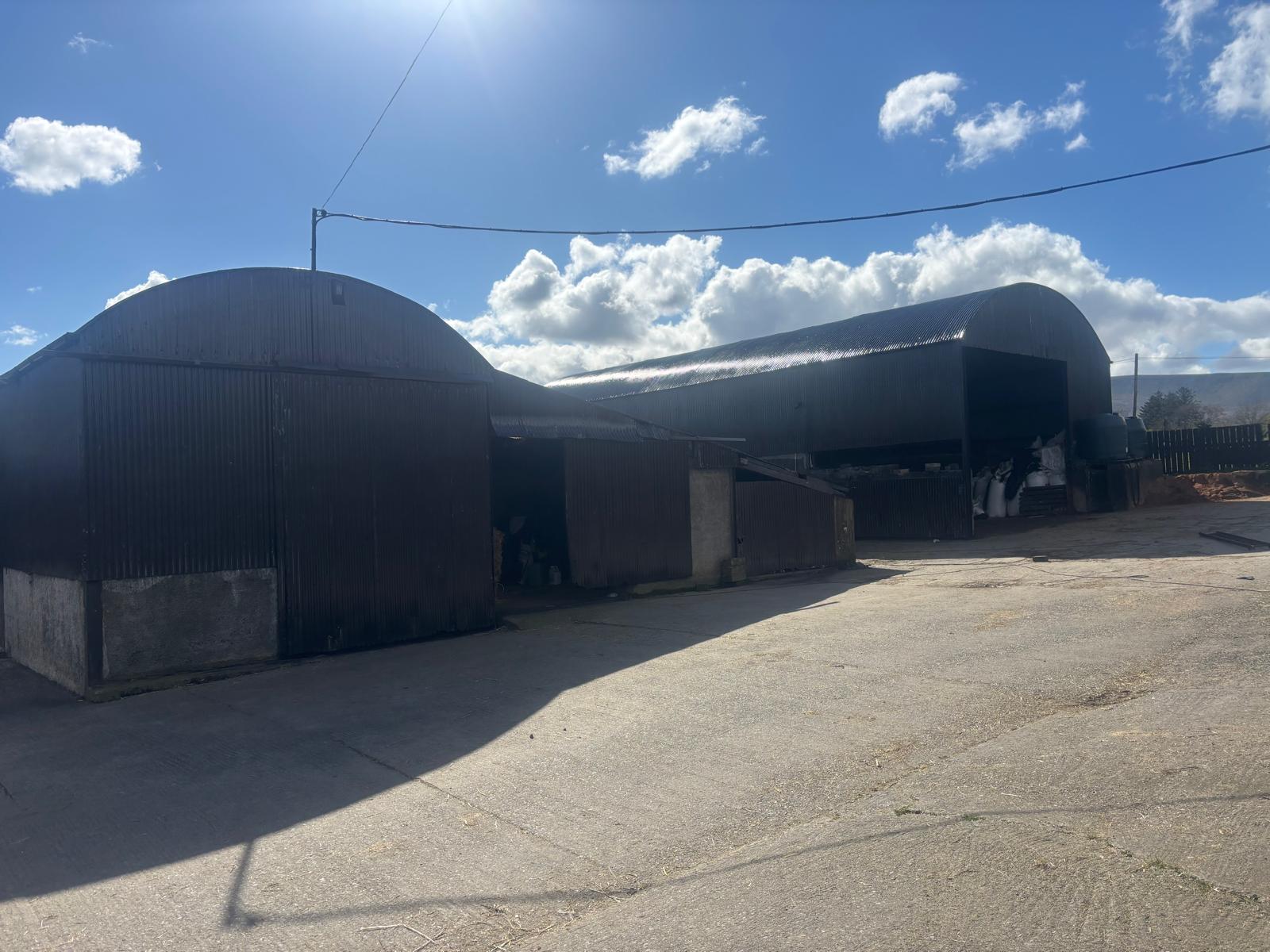 Two dark round-roof farm sheds on a sunny day